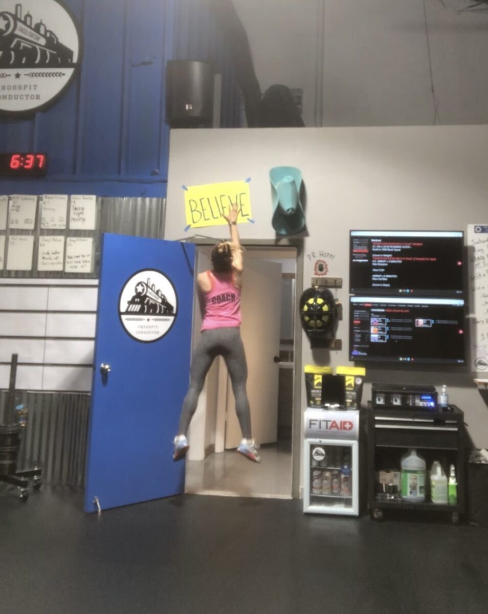 Amanda jumping in front of a BELIEVE sign